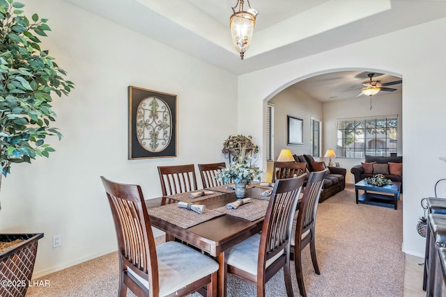 dining space featuring arched walkways, baseboards, light carpet, and a tray ceiling