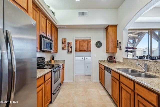 kitchen with a sink, visible vents, washer and dryer, appliances with stainless steel finishes, and light stone countertops