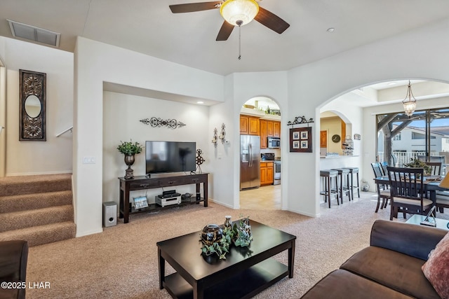 living area featuring arched walkways, light colored carpet, visible vents, stairway, and a ceiling fan