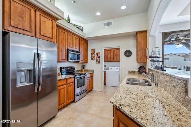 kitchen with a sink, visible vents, appliances with stainless steel finishes, light stone countertops, and washer / clothes dryer