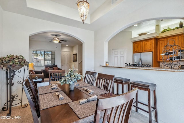 dining space with a ceiling fan, arched walkways, and a tray ceiling