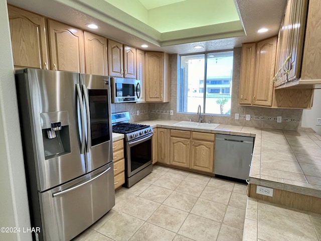 kitchen with appliances with stainless steel finishes, tile countertops, tasteful backsplash, sink, and a tray ceiling