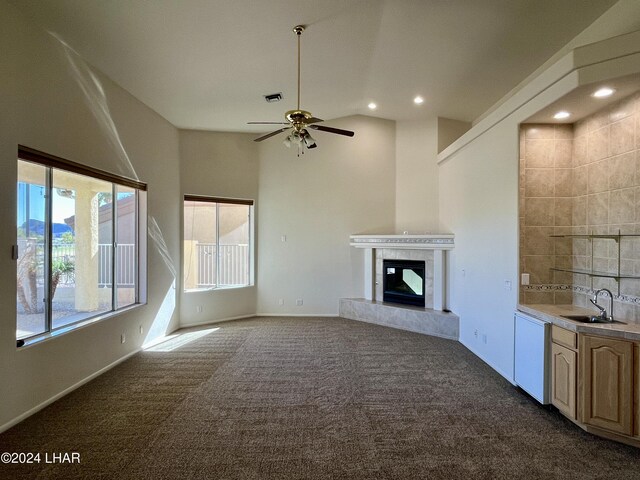 unfurnished living room with a tiled fireplace, dark colored carpet, sink, and ceiling fan