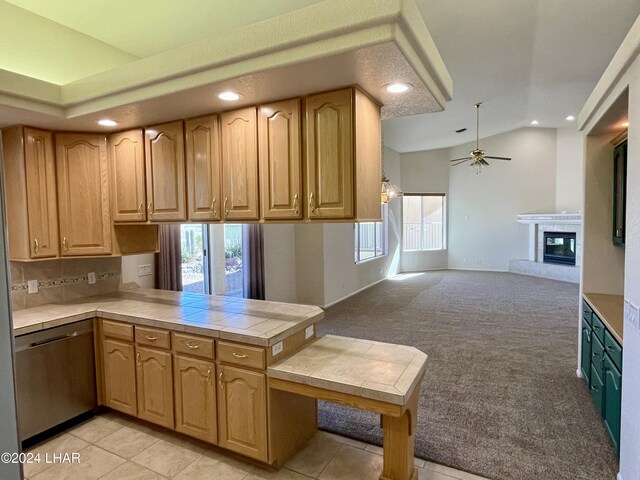 kitchen with lofted ceiling, dishwasher, tile counters, light colored carpet, and kitchen peninsula