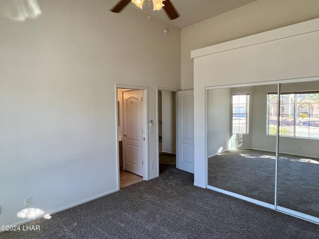 unfurnished bedroom featuring ceiling fan, a towering ceiling, dark carpet, and a closet