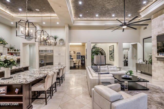 living area featuring ceiling fan with notable chandelier, a tray ceiling, ornamental molding, and a high ceiling