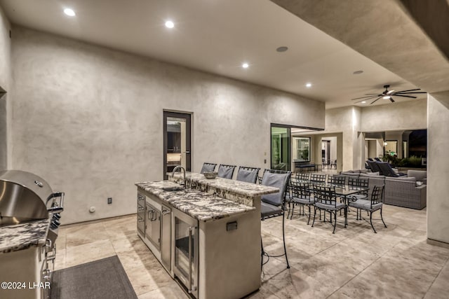 kitchen with light stone counters, an island with sink, a sink, and recessed lighting