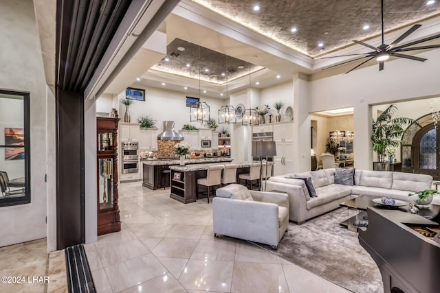 living area featuring a tray ceiling, recessed lighting, a towering ceiling, ornamental molding, and ceiling fan with notable chandelier