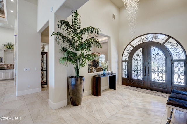 entryway featuring baseboards, french doors, a towering ceiling, and a notable chandelier