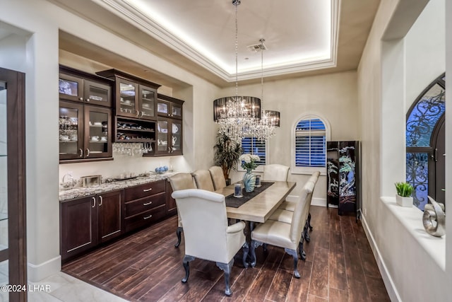 dining space with dark wood-type flooring, a raised ceiling, baseboards, and an inviting chandelier