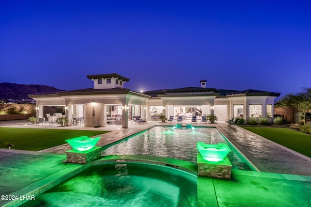 pool at twilight with a pool with connected hot tub and a patio area