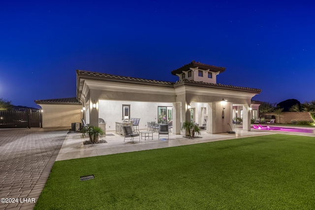 back of house at night with a patio, fence, a tile roof, a yard, and stucco siding