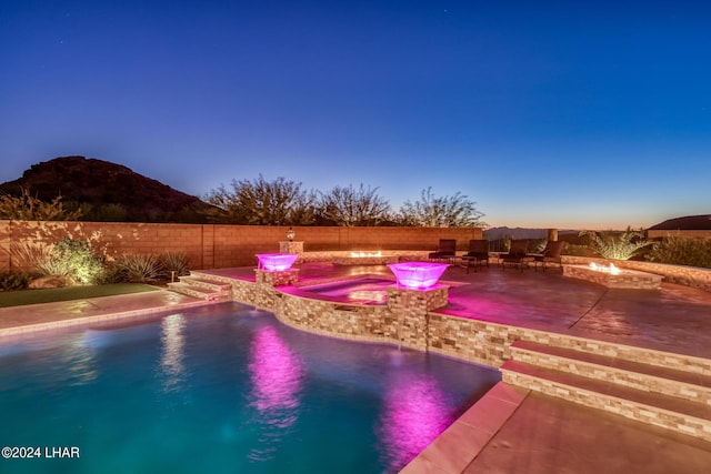 pool at dusk featuring a fire pit, a fenced in pool, a patio, a fenced backyard, and an in ground hot tub