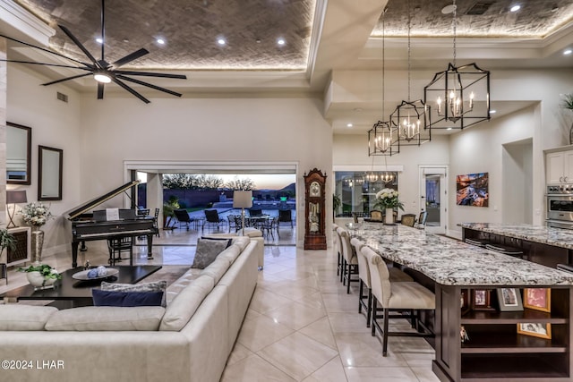 living room featuring light tile patterned floors, a high ceiling, visible vents, and ceiling fan with notable chandelier