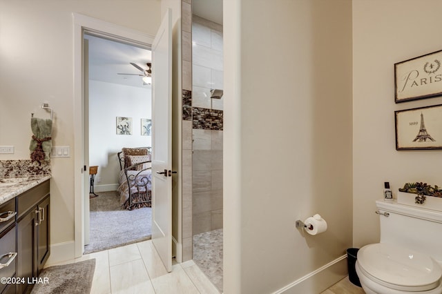 bathroom featuring toilet, ceiling fan, vanity, tiled shower, and baseboards