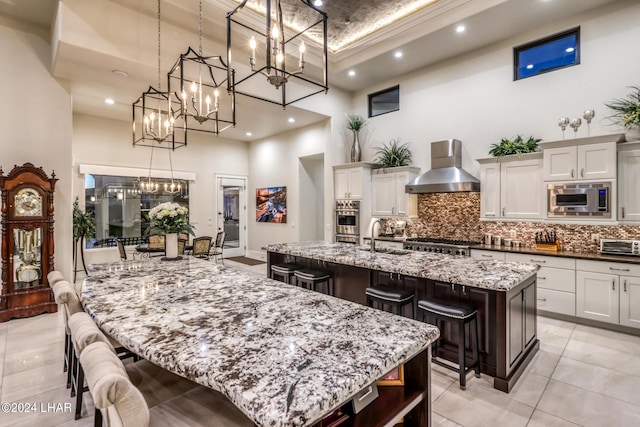 kitchen with appliances with stainless steel finishes, a large island, decorative backsplash, wall chimney exhaust hood, and a kitchen bar