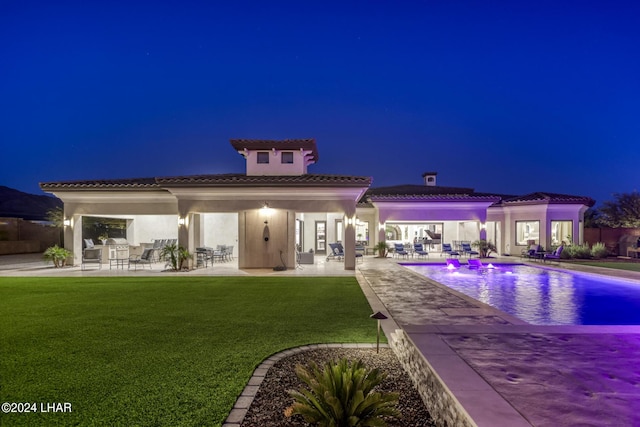 back of house at twilight featuring a yard, a patio, and stucco siding