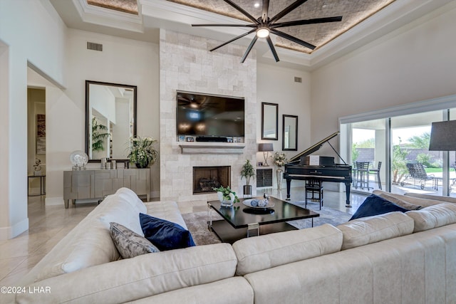 living area with a stone fireplace, visible vents, baseboards, ornamental molding, and a tray ceiling