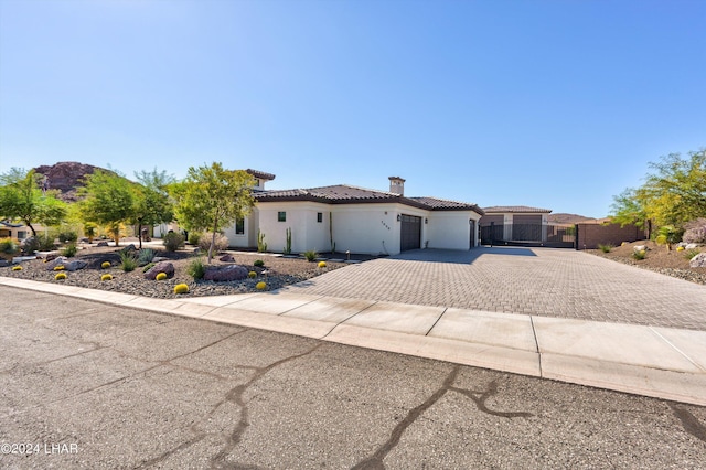 mediterranean / spanish home with a tile roof, decorative driveway, a gate, stucco siding, and a chimney