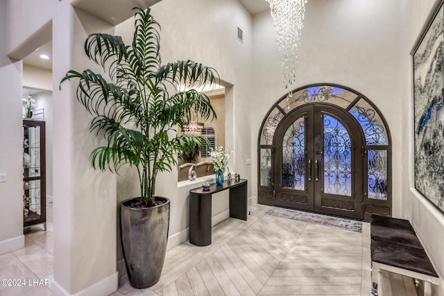 entryway with a notable chandelier, a towering ceiling, baseboards, visible vents, and french doors