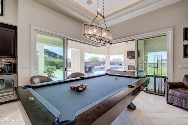 game room with a tray ceiling, wine cooler, ornamental molding, a glass covered fireplace, and a healthy amount of sunlight