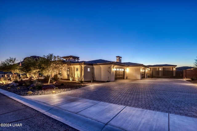 view of front of property with an attached garage, a tiled roof, decorative driveway, stucco siding, and a chimney