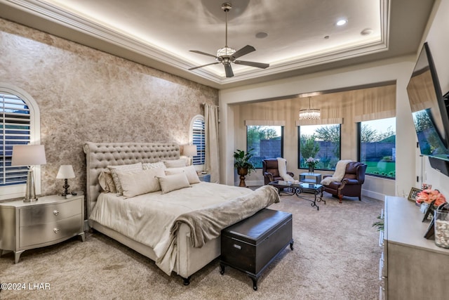 carpeted bedroom featuring ceiling fan with notable chandelier, a tray ceiling, and ornamental molding