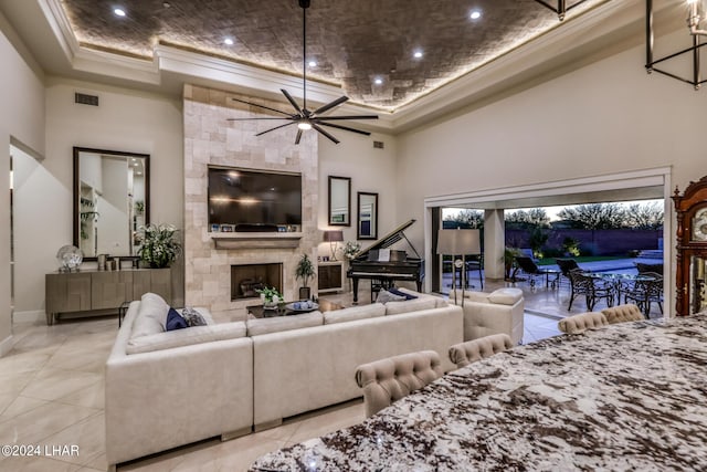 living area with a raised ceiling, visible vents, a high ceiling, ornamental molding, and a stone fireplace