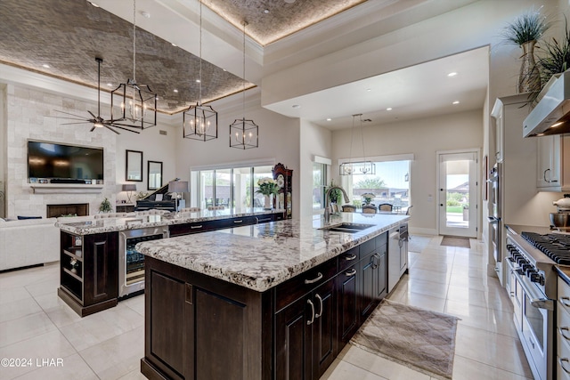 kitchen with beverage cooler, a large fireplace, a sink, hanging light fixtures, and a large island with sink