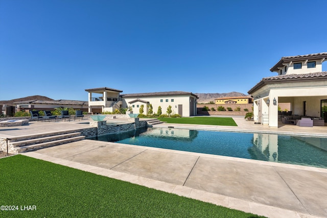 view of swimming pool featuring a mountain view, a pool with connected hot tub, a patio, and a lawn