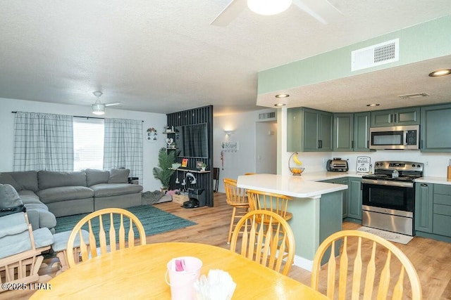 kitchen featuring visible vents, a ceiling fan, stainless steel appliances, a peninsula, and green cabinetry