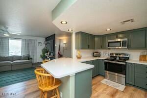 kitchen with a peninsula, stainless steel appliances, green cabinets, and a kitchen breakfast bar