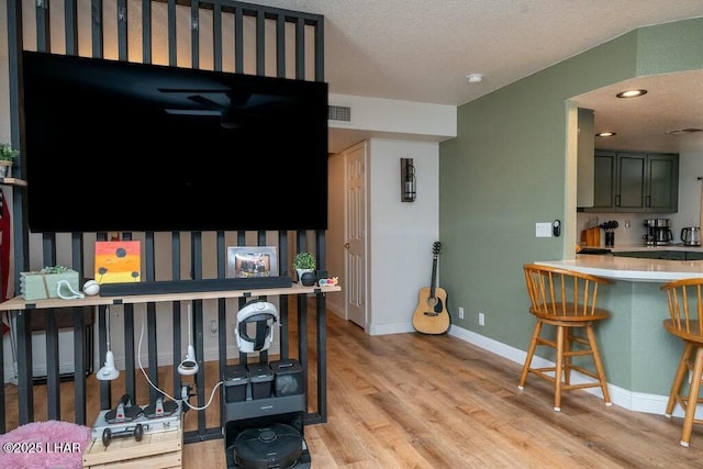 living room with visible vents, light wood-style floors, baseboards, and a textured ceiling