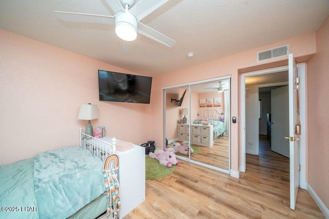 bedroom with a ceiling fan, wood finished floors, visible vents, baseboards, and a closet