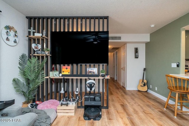 living area featuring a ceiling fan, wood finished floors, visible vents, baseboards, and a textured ceiling