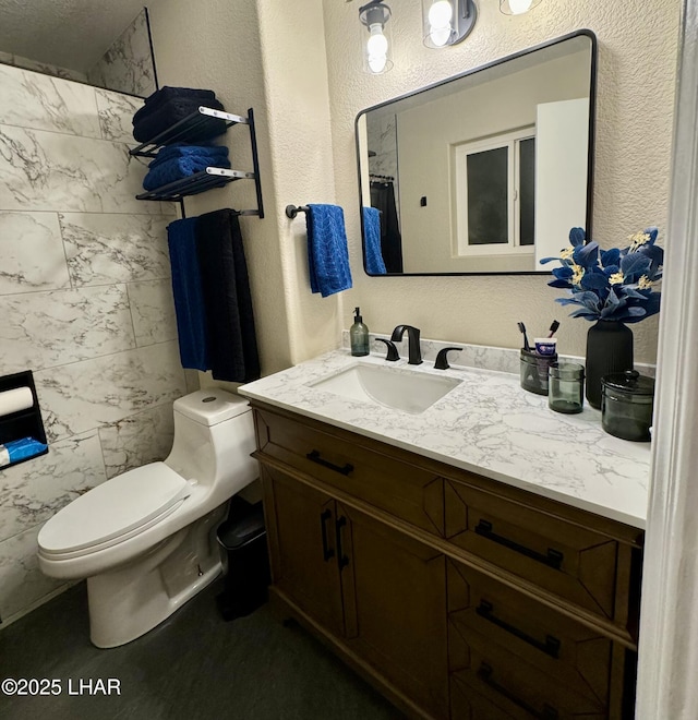 full bath with toilet, vanity, and a textured wall