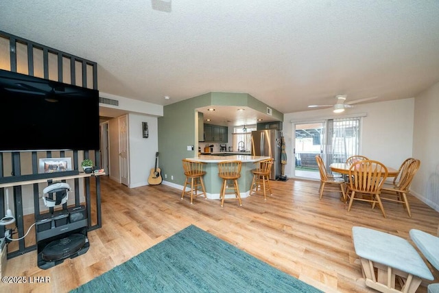 kitchen featuring freestanding refrigerator, light countertops, a textured ceiling, a kitchen bar, and light wood-type flooring