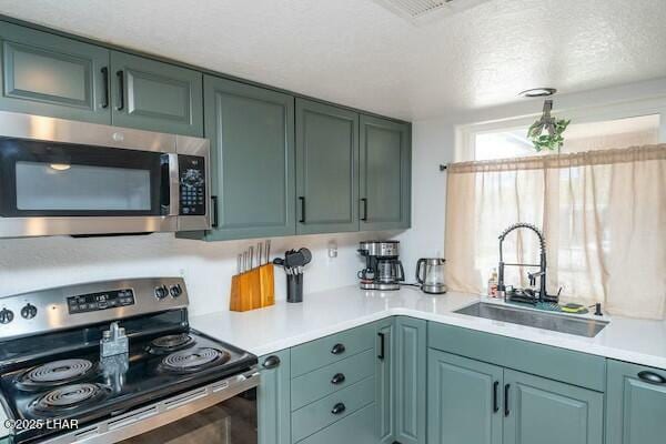 kitchen with a textured ceiling, light countertops, appliances with stainless steel finishes, and a sink