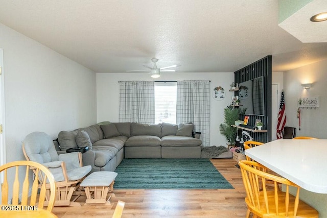 living room with a ceiling fan, light wood-type flooring, and a textured ceiling