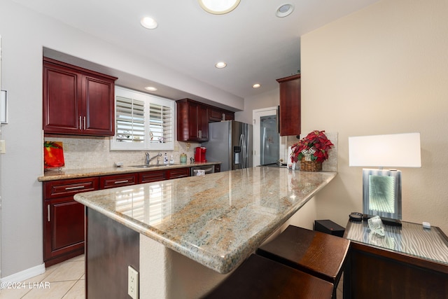 kitchen featuring light stone counters, a kitchen breakfast bar, a peninsula, stainless steel refrigerator with ice dispenser, and a sink