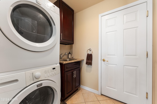 laundry area with stacked washer and dryer, cabinet space, baseboards, a sink, and light tile patterned flooring