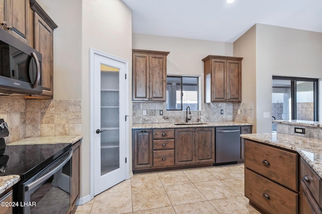 kitchen with sink, light tile patterned floors, appliances with stainless steel finishes, light stone counters, and decorative backsplash