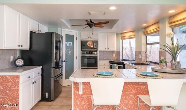 kitchen with white cabinetry, tile countertops, kitchen peninsula, and black appliances