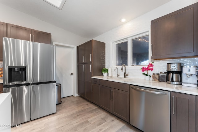 kitchen with sink, dark brown cabinets, stainless steel appliances, decorative backsplash, and light wood-type flooring