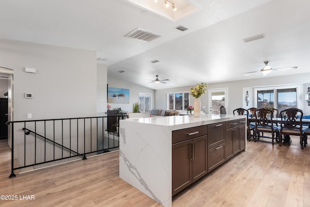 kitchen with dark brown cabinetry, light stone counters, vaulted ceiling, a large island, and light hardwood / wood-style floors