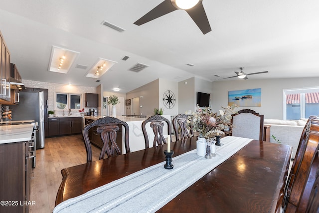 dining room with ceiling fan, lofted ceiling, sink, and light wood-type flooring