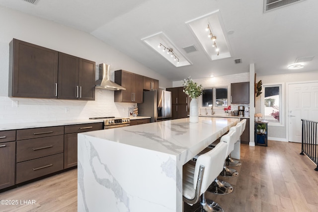 kitchen featuring a breakfast bar area, vaulted ceiling, a kitchen island, stainless steel appliances, and wall chimney range hood