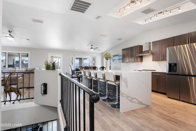 kitchen with lofted ceiling, stainless steel fridge, a center island, a kitchen bar, and wall chimney exhaust hood