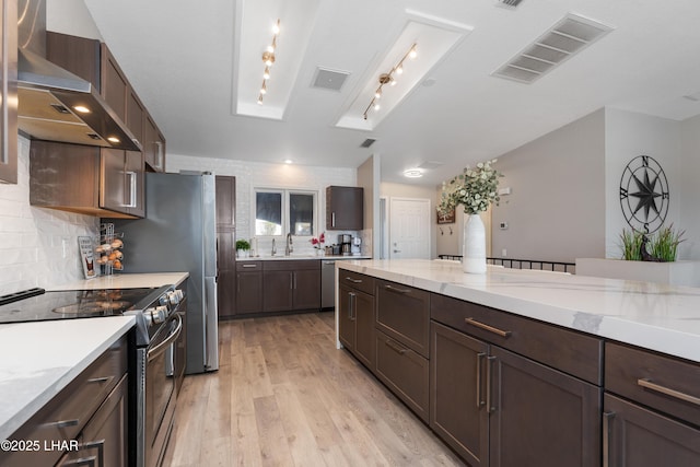 kitchen featuring ventilation hood, sink, stainless steel range with electric cooktop, decorative backsplash, and light wood-type flooring