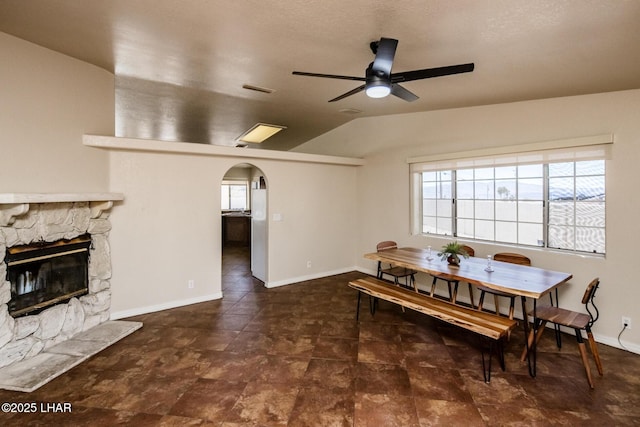 dining space featuring arched walkways, lofted ceiling, a fireplace, visible vents, and a ceiling fan